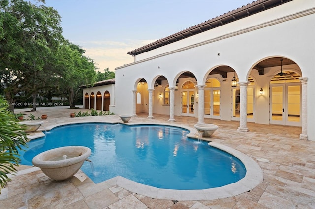 pool at dusk featuring pool water feature, french doors, and a patio