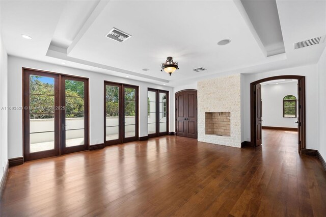 unfurnished living room with a stone fireplace, a tray ceiling, french doors, and dark hardwood / wood-style floors