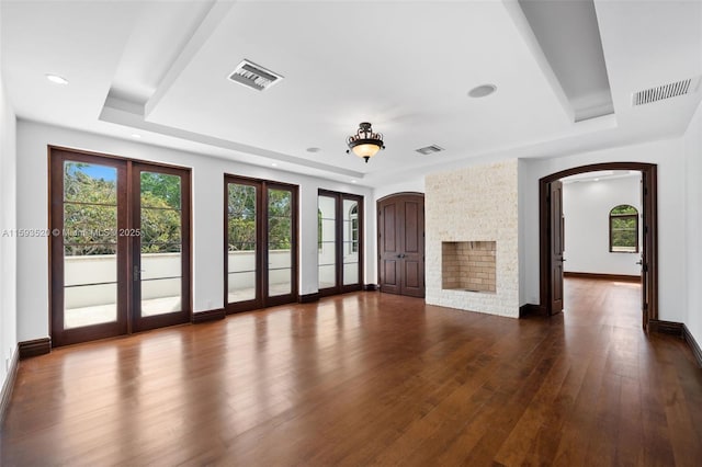 unfurnished living room featuring a raised ceiling, french doors, dark hardwood / wood-style flooring, and a fireplace