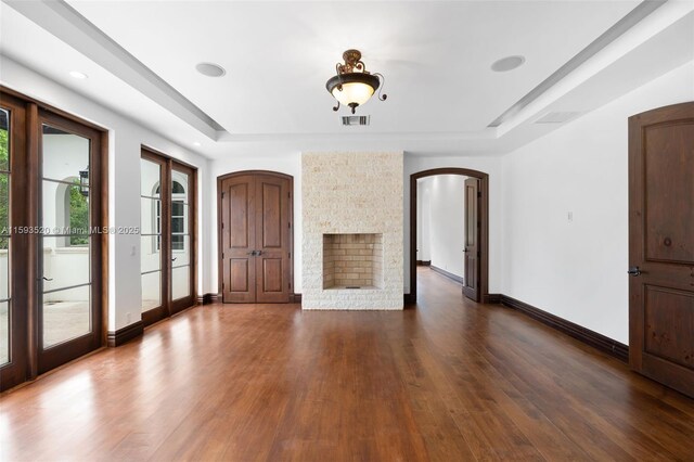 unfurnished living room featuring french doors, dark hardwood / wood-style floors, a raised ceiling, and a fireplace