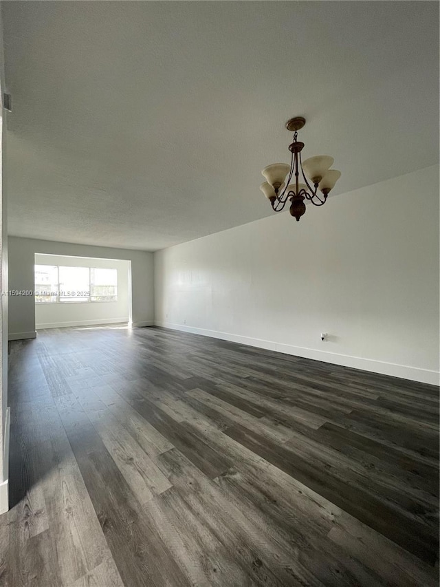 empty room featuring baseboards, dark wood-type flooring, and a chandelier