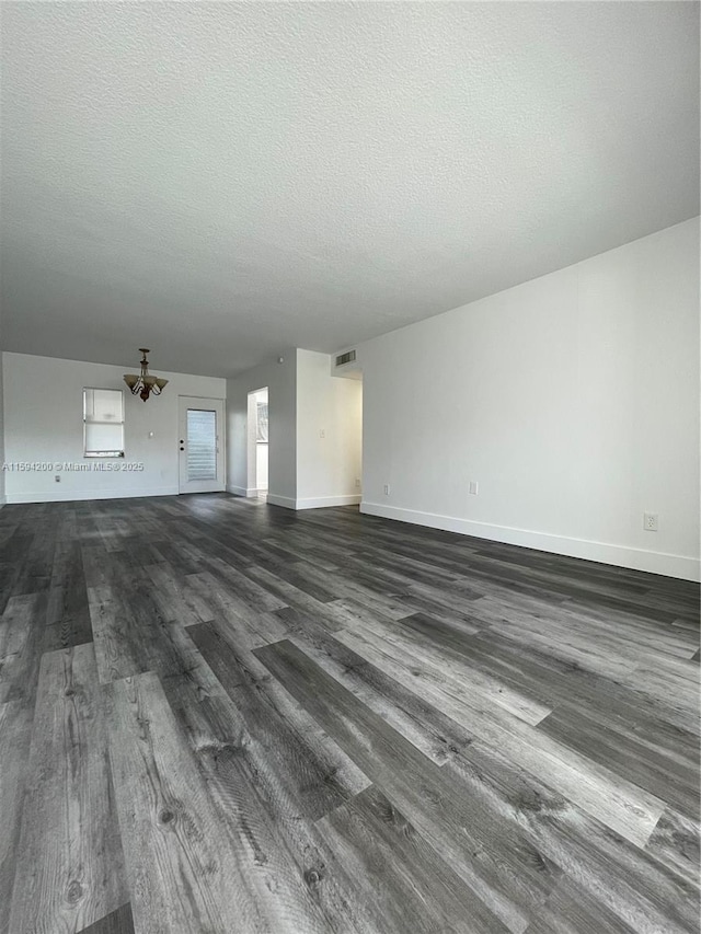 unfurnished living room featuring visible vents, baseboards, a textured ceiling, and dark wood-style floors