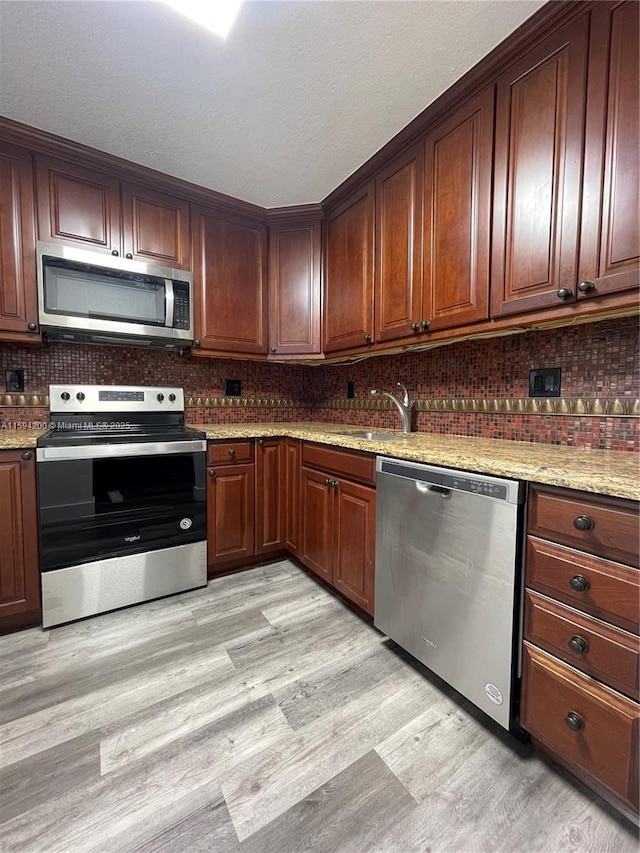 kitchen featuring tasteful backsplash, light stone counters, light wood-style flooring, stainless steel appliances, and a sink