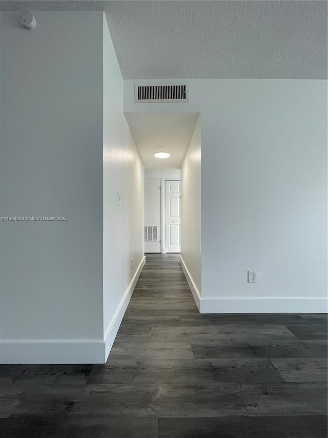 corridor featuring dark wood-type flooring, baseboards, visible vents, and a textured ceiling