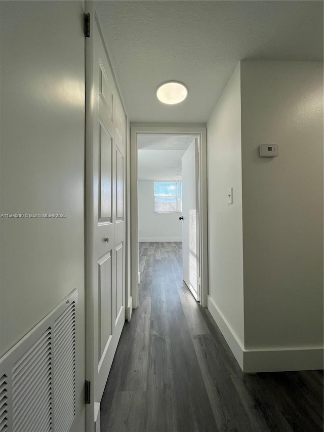 corridor featuring visible vents, a textured ceiling, dark wood-type flooring, and baseboards