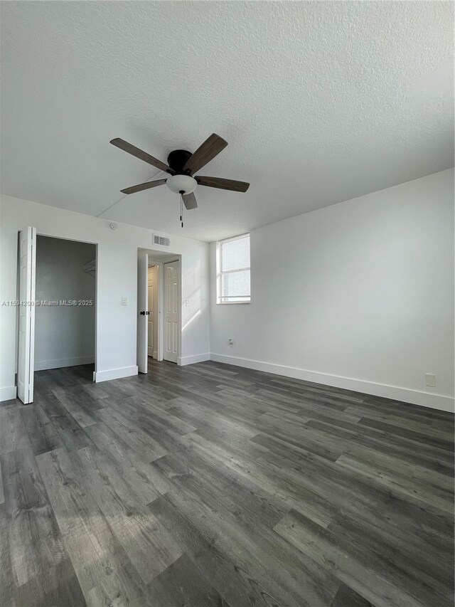 unfurnished bedroom featuring visible vents, baseboards, a textured ceiling, and dark wood-style flooring