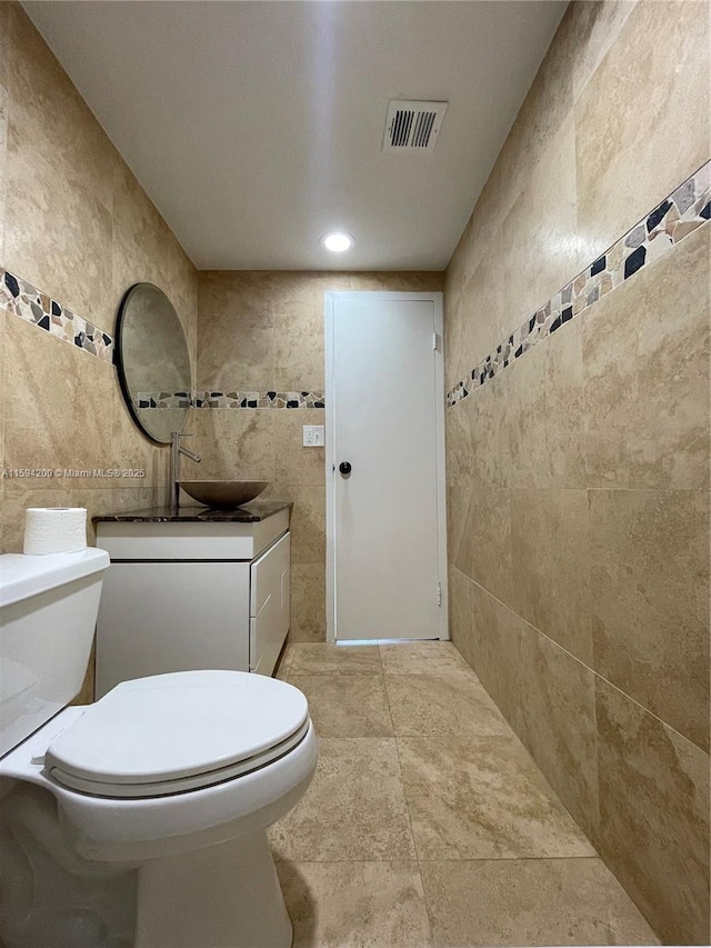 bathroom featuring vanity, tile walls, toilet, and visible vents