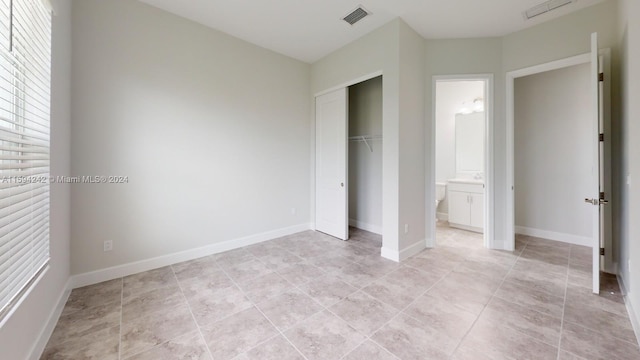 unfurnished bedroom with ensuite bathroom, a closet, and light tile floors