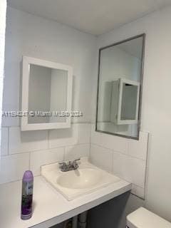 bathroom featuring vanity, backsplash, toilet, and tile walls