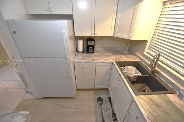 kitchen with white refrigerator, sink, backsplash, and white cabinetry