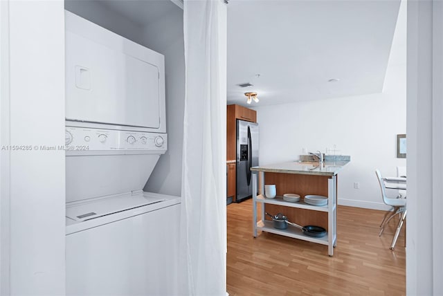 laundry area with stacked washing maching and dryer, sink, and light hardwood / wood-style floors