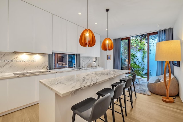 kitchen with backsplash, white cabinets, light hardwood / wood-style floors, and pendant lighting