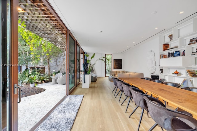 office area with floor to ceiling windows, built in shelves, and light hardwood / wood-style flooring