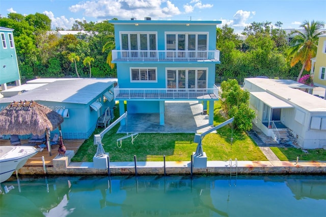 back of property with a water view, a patio, a balcony, and a lawn