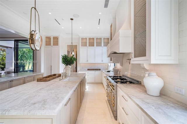 kitchen featuring range with two ovens, glass insert cabinets, a sink, custom exhaust hood, and backsplash