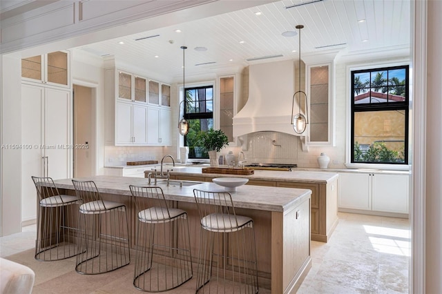 kitchen with white cabinetry, an island with sink, hanging light fixtures, and premium range hood