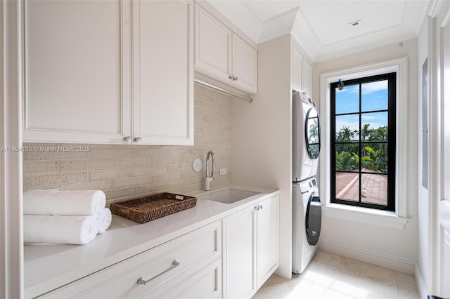 laundry room with stacked washer and dryer, cabinet space, baseboards, and a sink