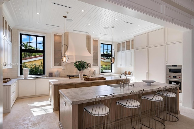 kitchen featuring tasteful backsplash, wood ceiling, a center island with sink, and a sink