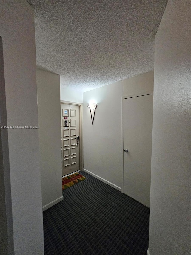 hallway with baseboards, dark colored carpet, and a textured ceiling