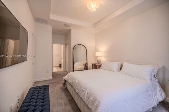 carpeted bedroom with a tray ceiling and ensuite bath