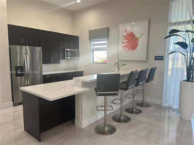 kitchen with light stone counters, stainless steel appliances, backsplash, a kitchen bar, and light tile floors