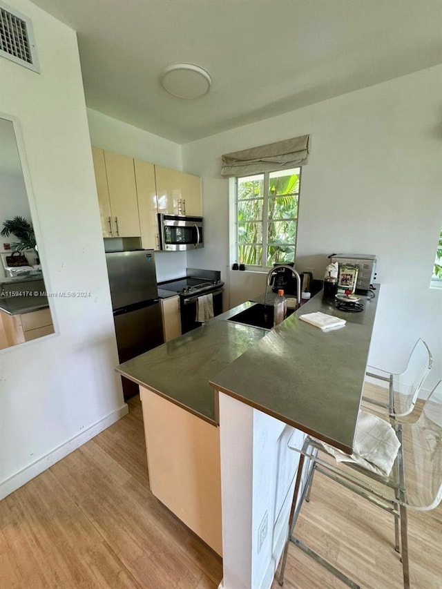 kitchen featuring appliances with stainless steel finishes, sink, kitchen peninsula, light hardwood / wood-style floors, and cream cabinetry