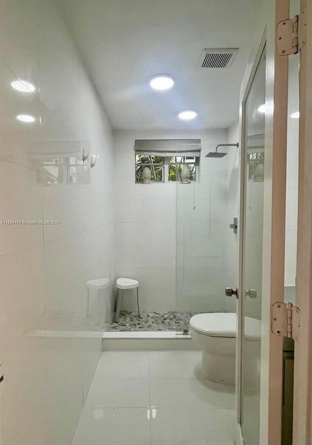 bathroom featuring toilet, a shower with door, tile patterned flooring, and tile walls