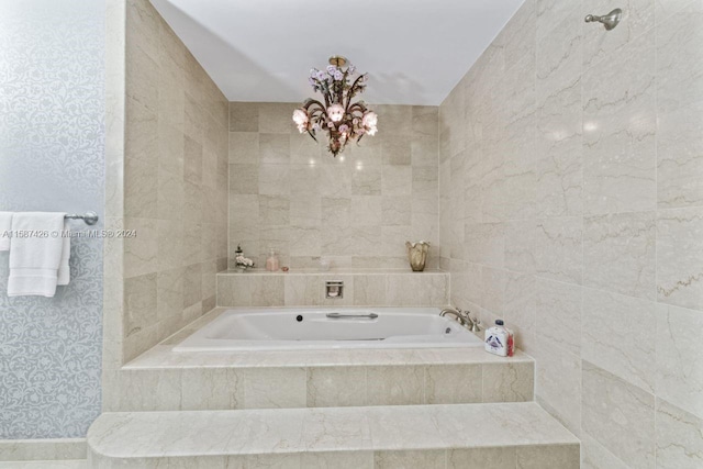 bathroom featuring an inviting chandelier and tiled bath