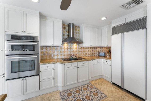 kitchen featuring backsplash, paneled built in refrigerator, wall chimney exhaust hood, stainless steel double oven, and light tile floors