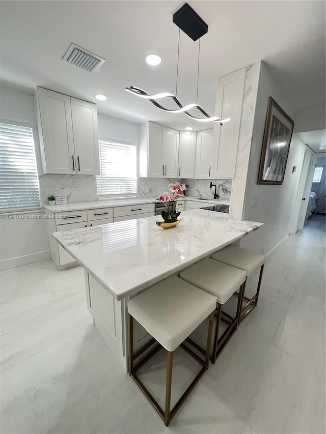 kitchen with decorative light fixtures, a kitchen island, white cabinetry, and light stone counters