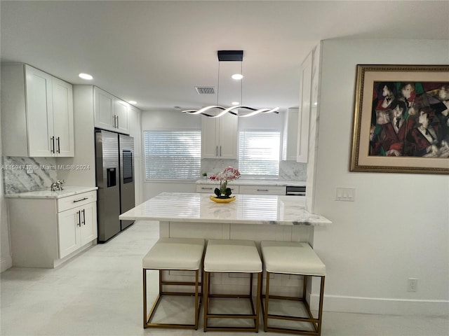 kitchen with a breakfast bar, white cabinets, stainless steel fridge, tasteful backsplash, and light stone counters