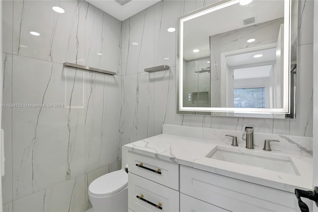 bathroom featuring vanity, tile walls, and toilet