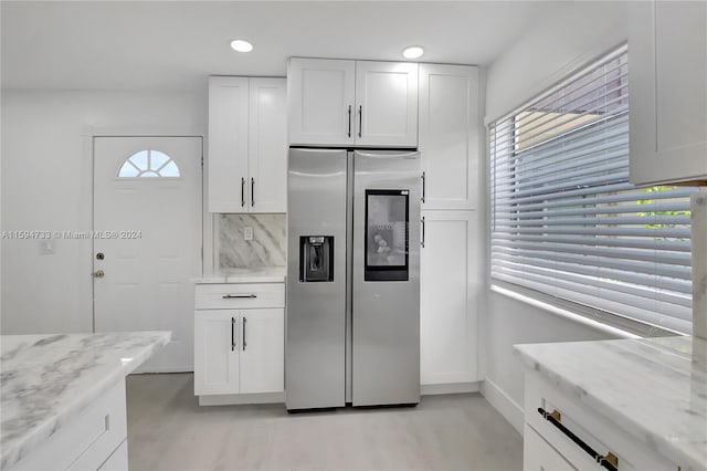 kitchen with white cabinets, stainless steel fridge with ice dispenser, backsplash, and light stone counters