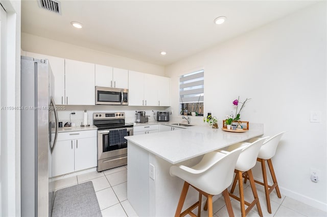 kitchen with white cabinetry, stainless steel appliances, kitchen peninsula, a breakfast bar, and light tile patterned floors