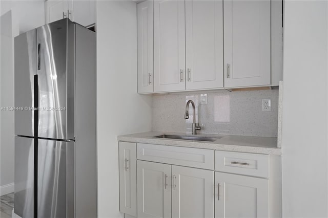 kitchen featuring stainless steel fridge, sink, light stone counters, backsplash, and white cabinetry