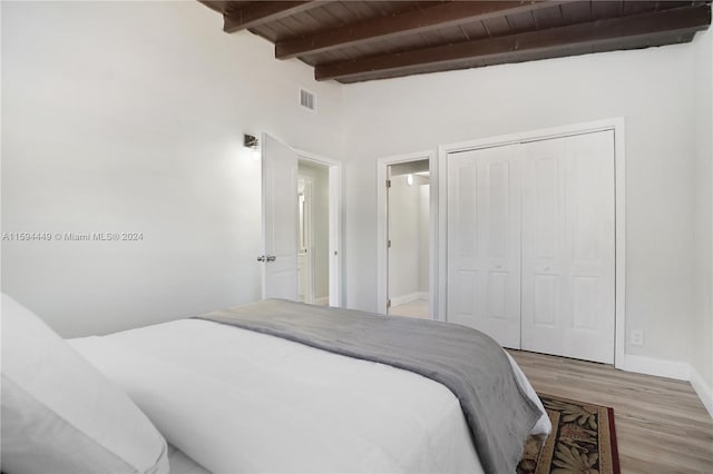 bedroom featuring beam ceiling, wood ceiling, a closet, and light wood-type flooring