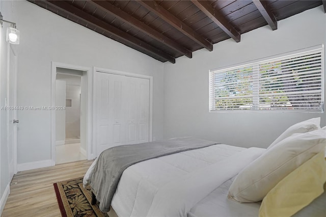 bedroom with connected bathroom, vaulted ceiling with beams, light hardwood / wood-style floors, wooden ceiling, and a closet