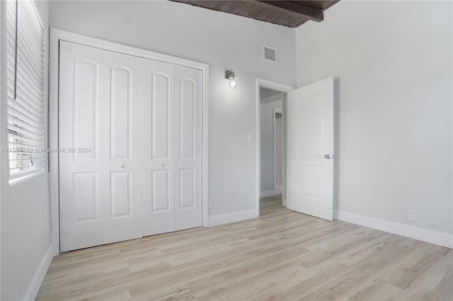 unfurnished bedroom with wood ceiling, light hardwood / wood-style floors, a closet, and vaulted ceiling with beams