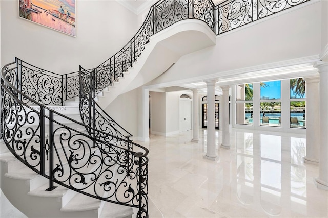 entryway with ornamental molding, a towering ceiling, and decorative columns