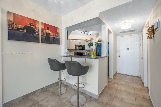 kitchen with a textured ceiling, a breakfast bar area, kitchen peninsula, and dark stone counters