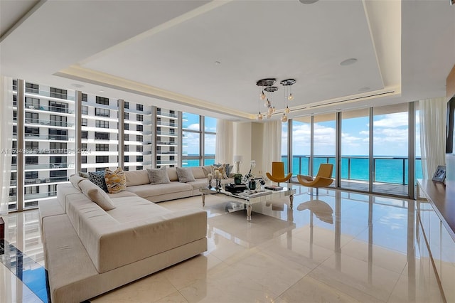 tiled living room with a chandelier, a wall of windows, a water view, and a raised ceiling