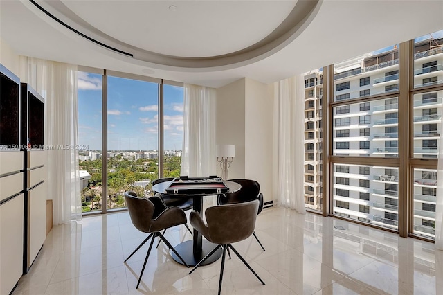 dining space featuring a raised ceiling, light tile flooring, and a wall of windows