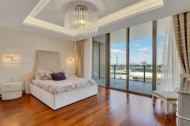 bedroom featuring a tray ceiling, access to exterior, hardwood / wood-style floors, a wall of windows, and a notable chandelier