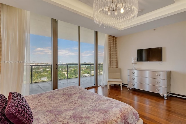 bedroom featuring an inviting chandelier, access to outside, expansive windows, a raised ceiling, and wood-type flooring