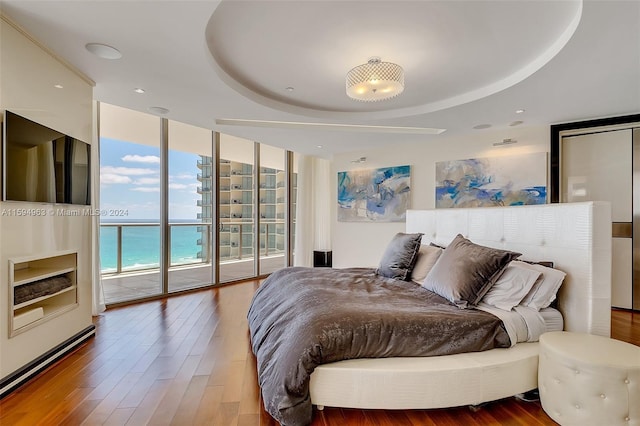 bedroom with wood-type flooring, a water view, a wall of windows, and access to outside