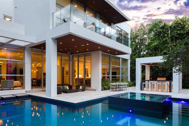 pool at dusk featuring an in ground hot tub and an outdoor bar