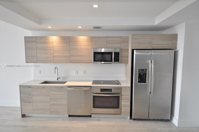 kitchen featuring appliances with stainless steel finishes, sink, light wood-type flooring, and a raised ceiling