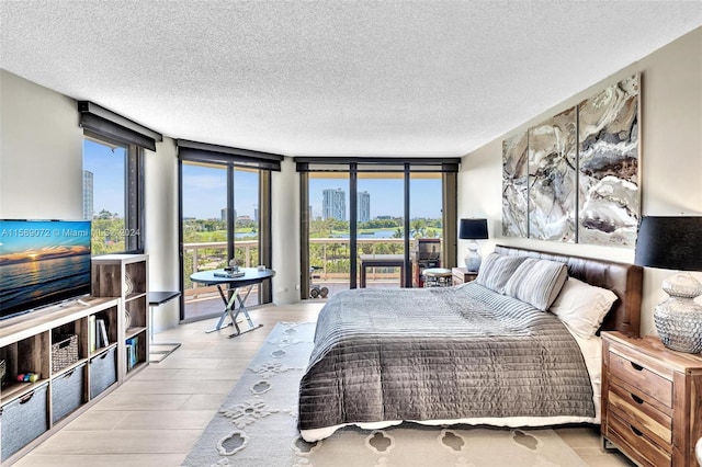 bedroom with access to outside, light hardwood / wood-style floors, expansive windows, and a textured ceiling