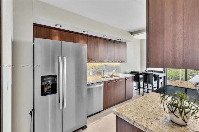 kitchen featuring sink, light tile patterned floors, appliances with stainless steel finishes, tasteful backsplash, and light stone countertops