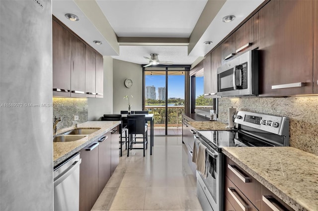 kitchen with sink, decorative backsplash, stainless steel appliances, and light stone countertops